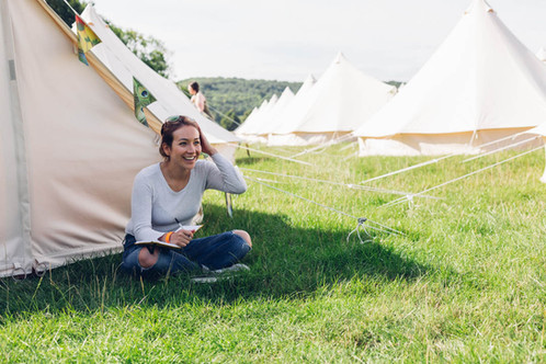 Young girl, bell tent, festival, music festival, girl sitting by a tent, girl with journal, notebook, journal, event photographer, festival , festival photographer, row of tents, teepee, tents, camping, yurts, yurt, photoshoot. brand photography, social media content, influencer photography, shooting in RAW, RAW editing, colour grading, commercial photography.