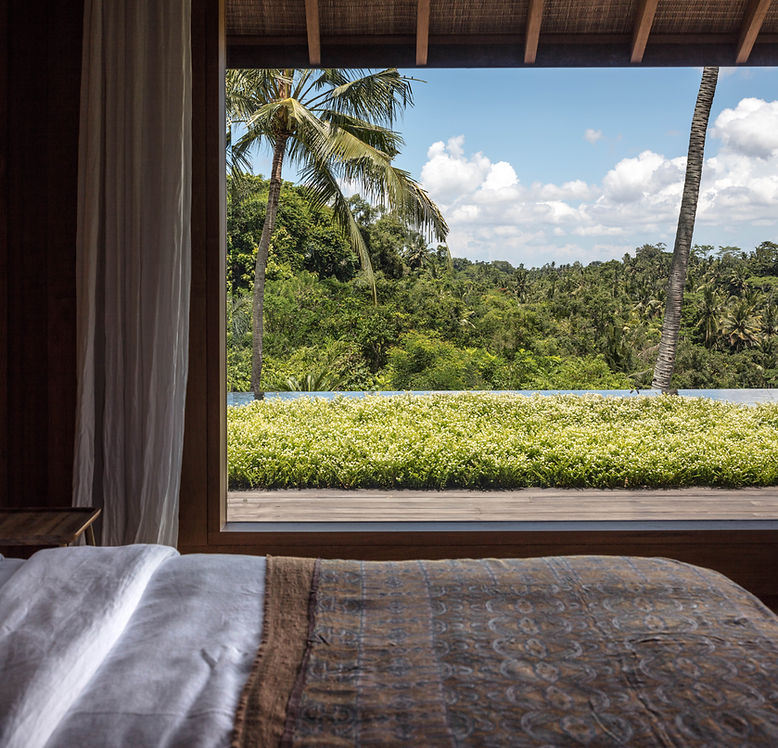 Tropical modernism luxury architectural photography of a private estate in Bali by Studio Jencquel. Highlighting the seamless indoor-outdoor living experience, raw organic materiality including rich teak wood and natural stone, and the interplay of lush jungle foliage with warm, dappled sunlight.