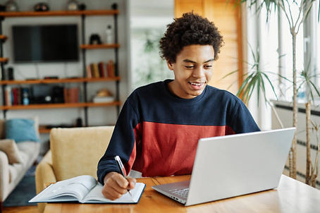 teen student doing homework on laptop, writing in notebook.jpg
