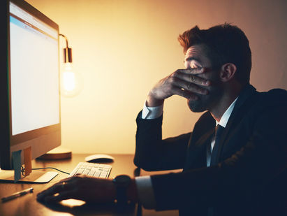 Exhausted business owner dealing with late-night tech problems and system issues, highlighting the stress of outgrowing a basic IT setup.