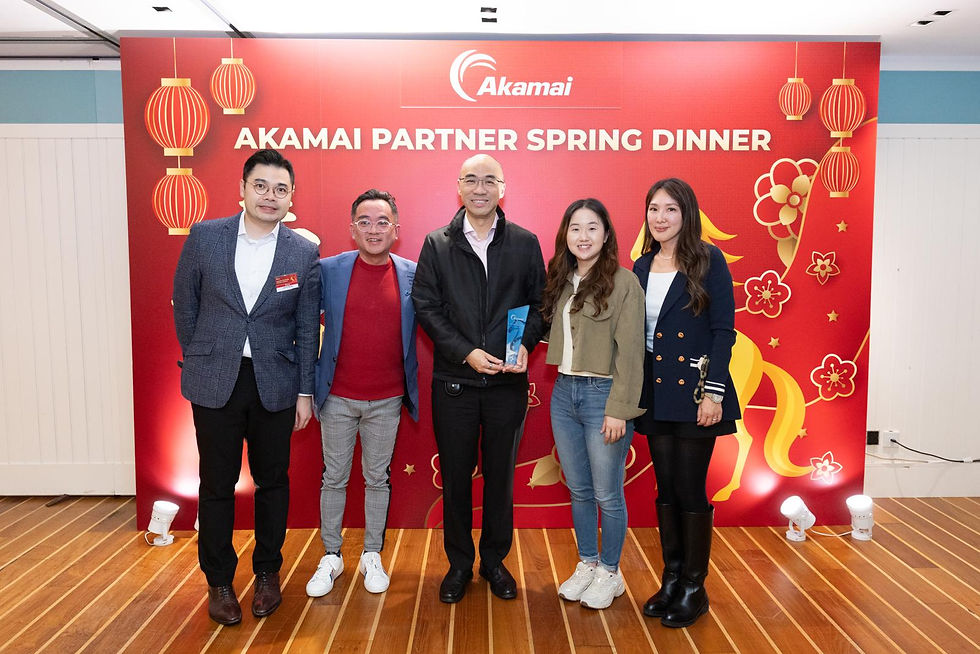 Group photo of event attendees at ‘Akamai Partner Spring Dinner’ standing before the branded red backdrop; one attendee holds a crystal partner award.