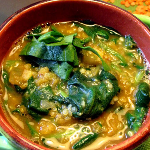 Piatto di quinoa con lenticchie e spinaci, condito con crema al limone e tahina, guarnito con semi di zucca e prezzemolo fresco; ricetta vegana ricca di ferro, colorata e nutriente.