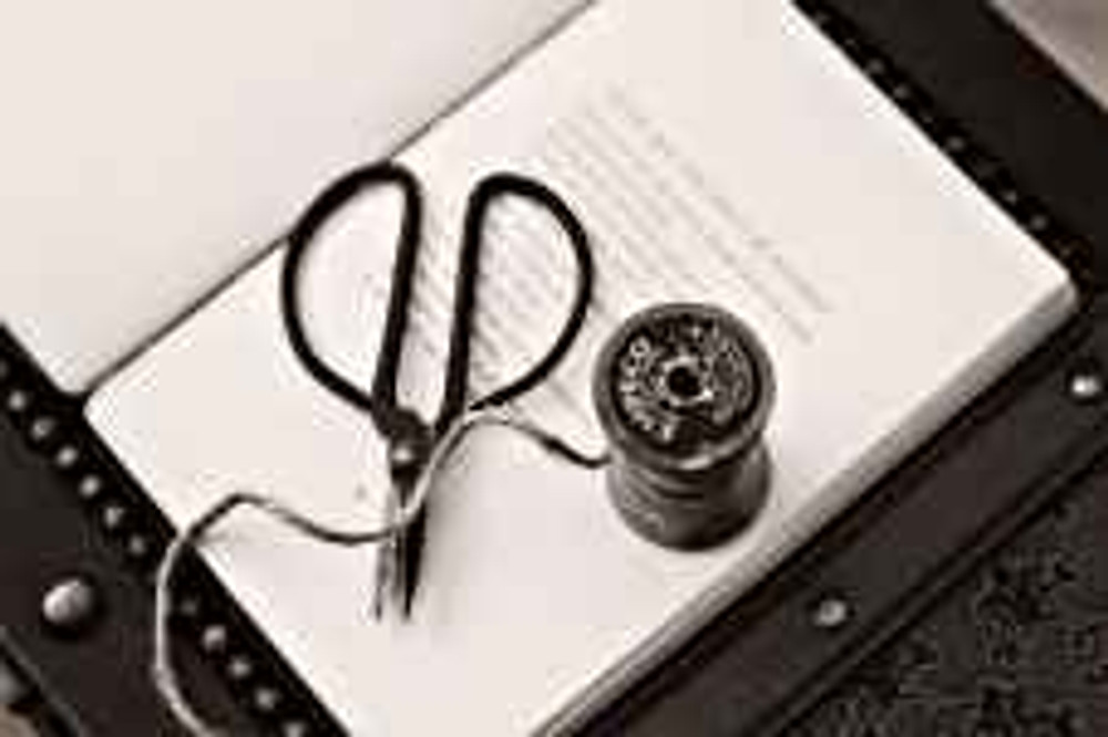 black scissors near thread reel on white book page