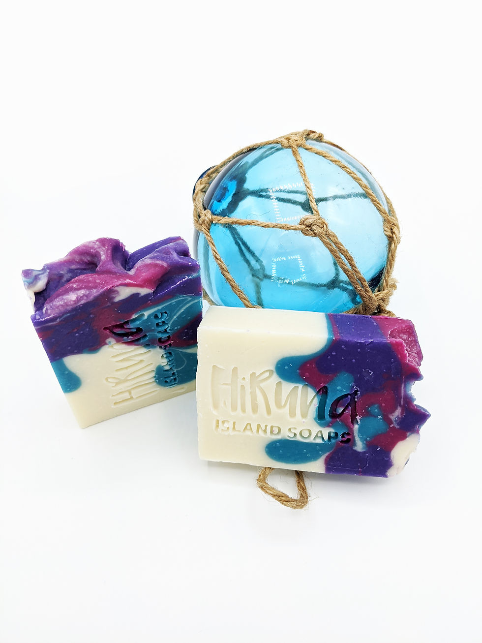 Thumbnail: Two bars of purple/pink/blue soap laying horizontally on a white background with a blue orb behind them