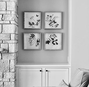 four frames with paper sculptures inside mounted on a wall. They are hung in an alcove of a living room with cupboard doors under the frames, a stone wall to one side and the top of a sofa visible in the foreground.