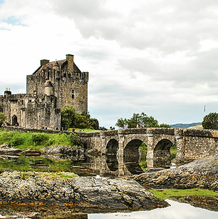 Stone castle and arched bridge reflected in calm water in the Scottish Highlands
