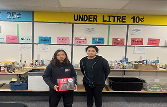 Two individuals stand in a recycling center, holding a red box