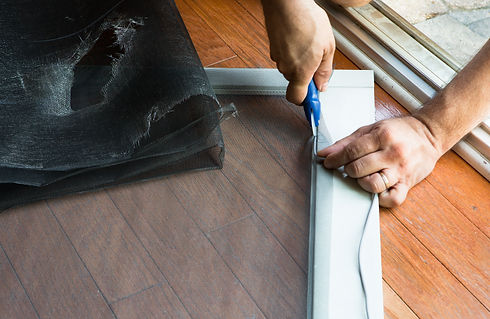 Hands repairing a torn window screen on a wooden floor
