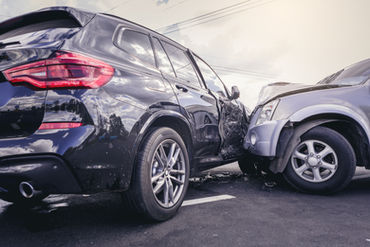 Two SUVs are involved in a collision on the road, with the front of a silver SUV impacting the side of a black SUV