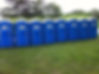 A row of blue portable toilets is lined up on a grassy field