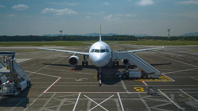 A parked airplane with a boarding ramp leading to the door sits on an airport tarmac