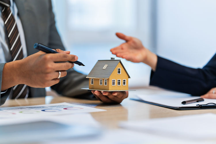 Hands hold a small house model over a desk with documents