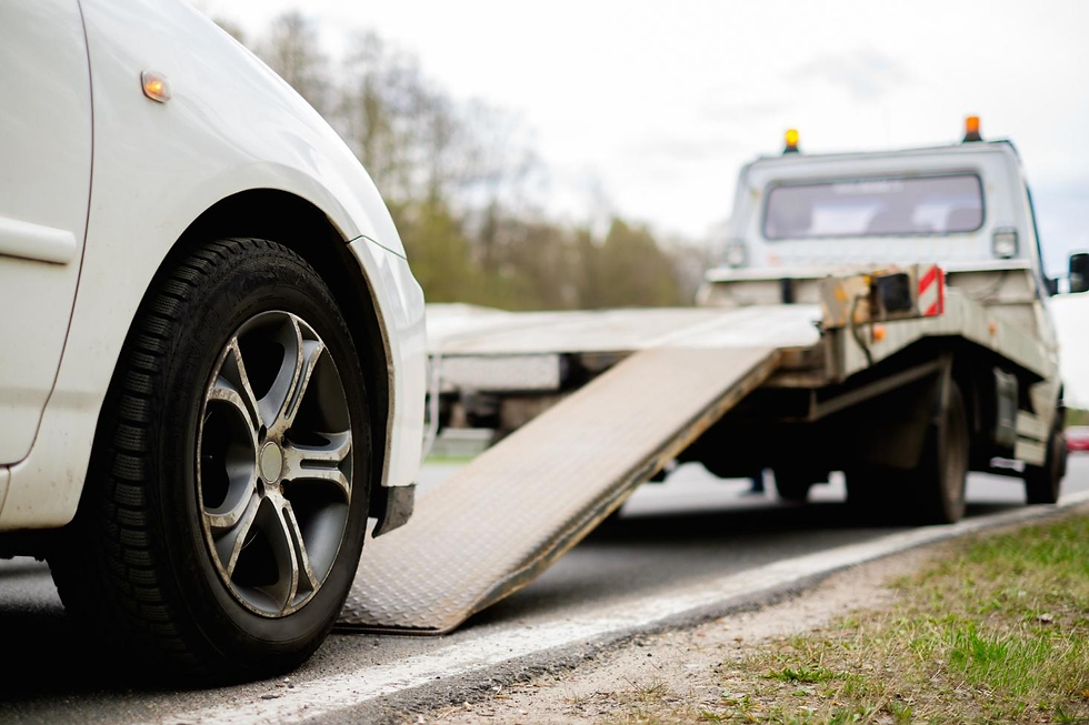 A white car positioned next to a tow truck with an extended loading ramp on a roadside