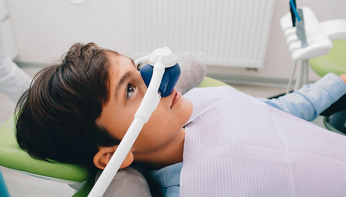 A child in a dentist chair wearing a nasal mask for sedation