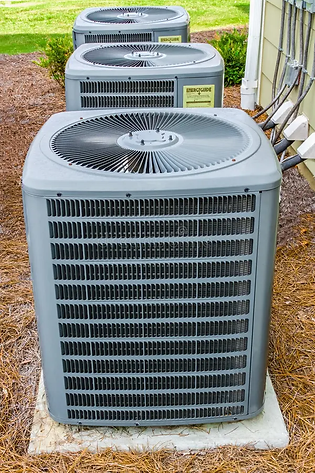 Three outdoor air conditioning units are lined up on concrete pads beside a building
