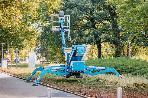 A blue spider lift on a grassy area, extended with stabilizing legs and an elevated platform