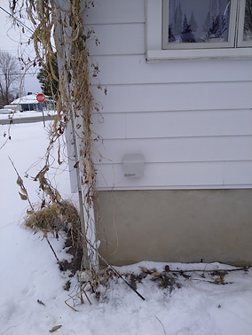 A white house corner with a small gray device mounted on the wall