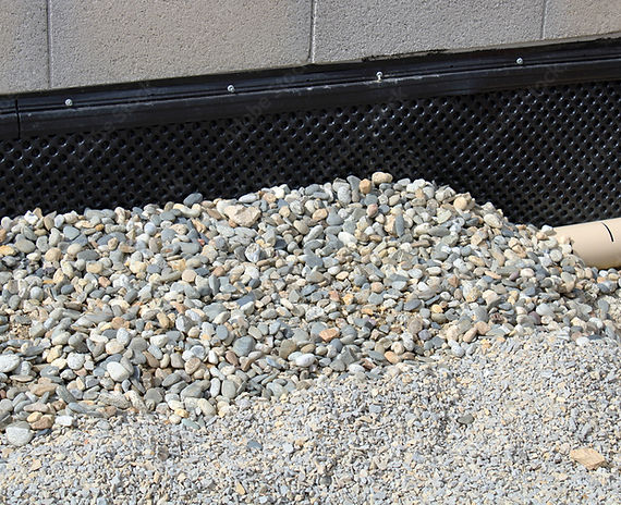 Un système de drainage avec de petites pierres lisses recouvrant un tuyau près d'un mur de bâtiment