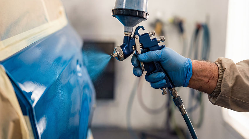 A person wearing blue gloves spray-paints a car door