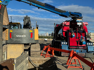 Construction site under a blue sky with a Volvo excavator and bright red industrial truck