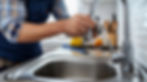 Close-up of a plumber's hands fixing a kitchen faucet above a stainless steel sink