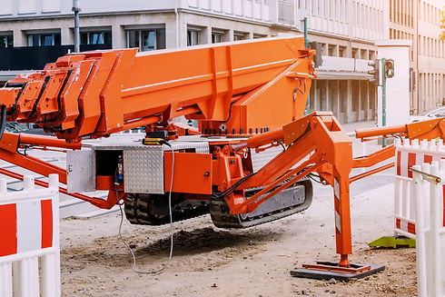 A bright orange construction lift with extended supports sits on a sandy street corner