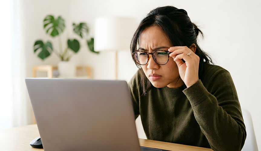 A woman wearing glasses leans forward, squinting at a laptop screen with a focused expression