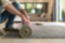 A person rolls out a gray carpet on a wooden floor in a cozy living room