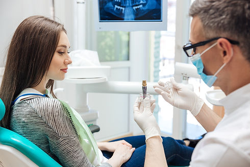A dentist in a mask shows a patient a dental implant model
