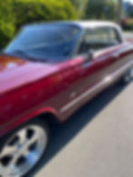 A shiny, vintage maroon car with sleek chrome wheels is parked