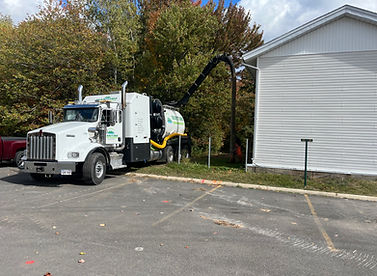 A white utility truck with a vacuum hose extends towards a white building