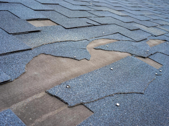 View of shingle roof damage that needs repair after a storm