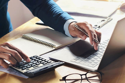 Une personne en costume bleu utilise une calculatrice et un ordinateur portable, tenant un stylo