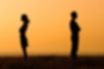 Silhouette of a couple standing feet apart in a field turned their backs to each other
