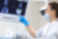 A dentist in a mask and gloves examines dental X-rays on a monitor