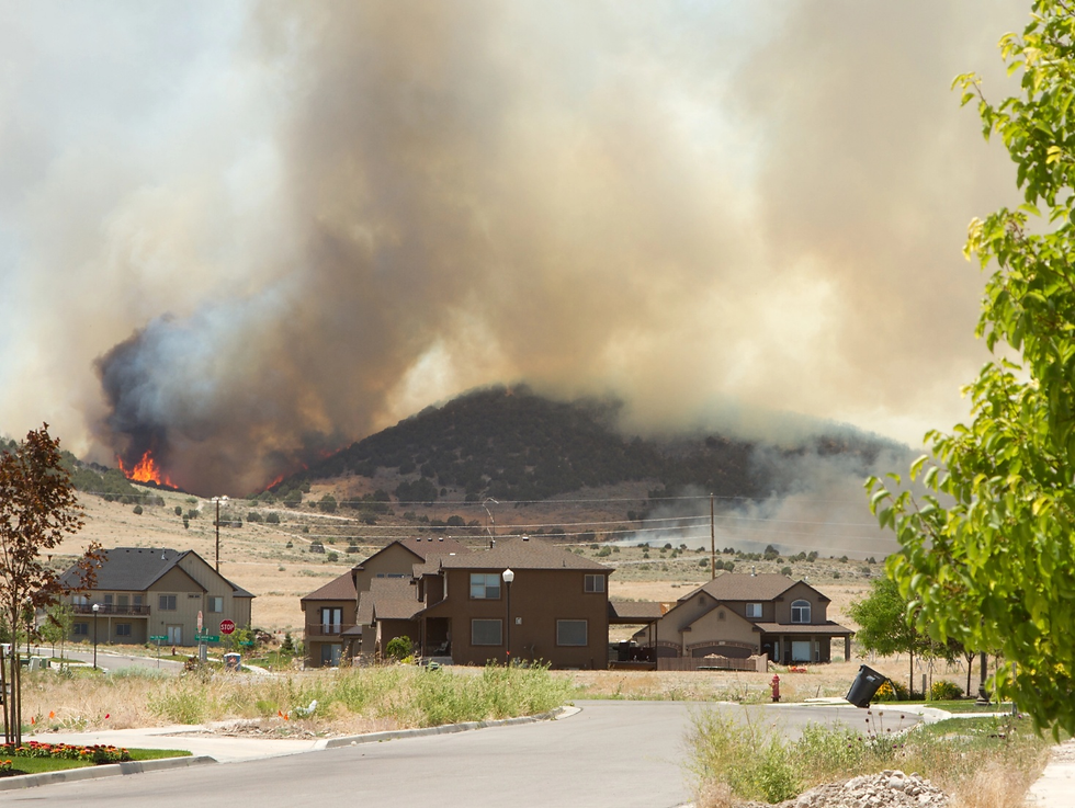 Wildfire burning near residential neighborhood with thick smoke approaching homes