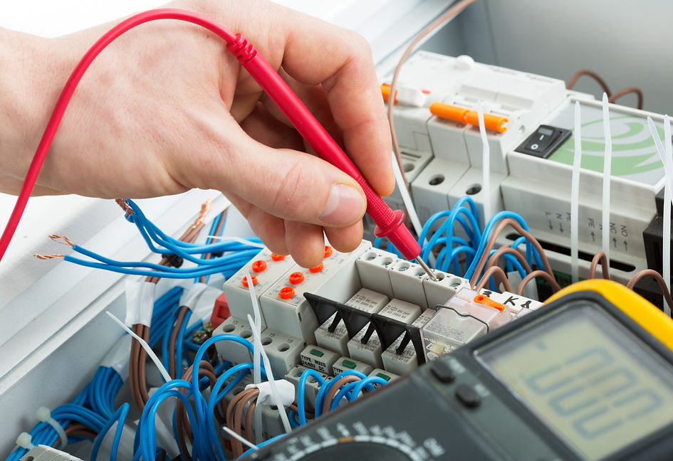 A hand is using a red probe to test electrical wires in a control panel filled with blue and brown cables
