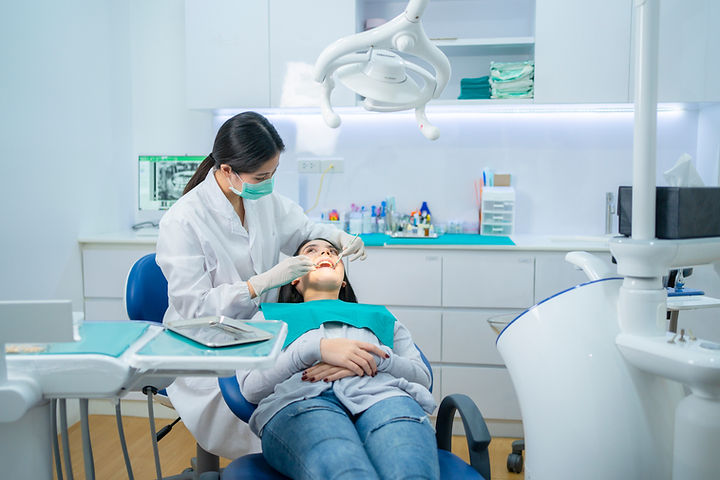Dentist in a white coat and mask examines a patient's teeth in a modern dental clinic