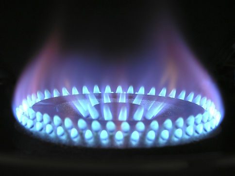Close-up of a lit gas stove burner with blue flames forming a ring pattern against a dark background