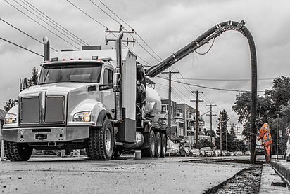 A large truck uses an extended hose for roadwork on a cloudy day