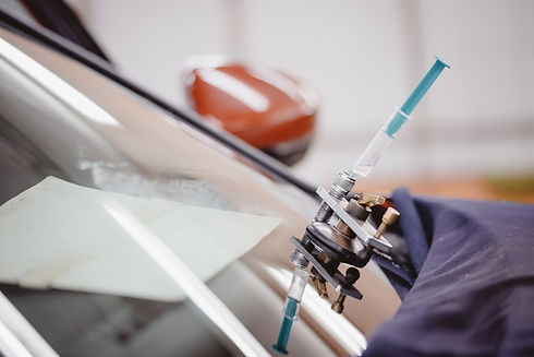 A windshield repair kit is attached to a car's cracked glass, with a syringe inserted