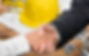 Handshake over blueprints and tools, with a yellow hard hat in the background