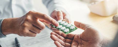 A doctor in a white coat hands a blister pack of pills to a patient's open hand