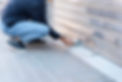 A person in jeans and a dark sweater squats on a tiled sidewalk, unlocking a metal shutter with a key