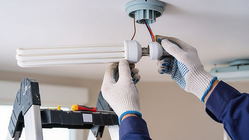 A person wearing white gloves upgrades a ceiling light bulb while standing on a ladder
