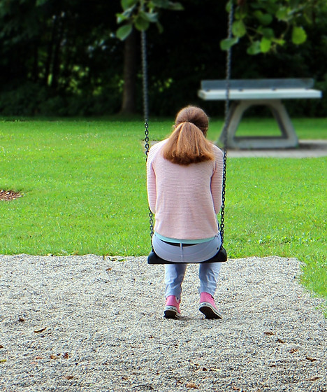 A young girl sits sadly on a swing with a bowed head