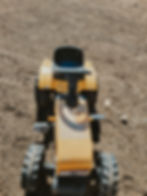 Toy tractor on a dirt ground, viewed from above. It's yellow with black wheels, creating a playful and rustic scene.