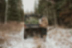 Woman and child by an ATV with a pine tree in a snowy forest. They wear winter clothes, conveying a cozy, adventurous mood.