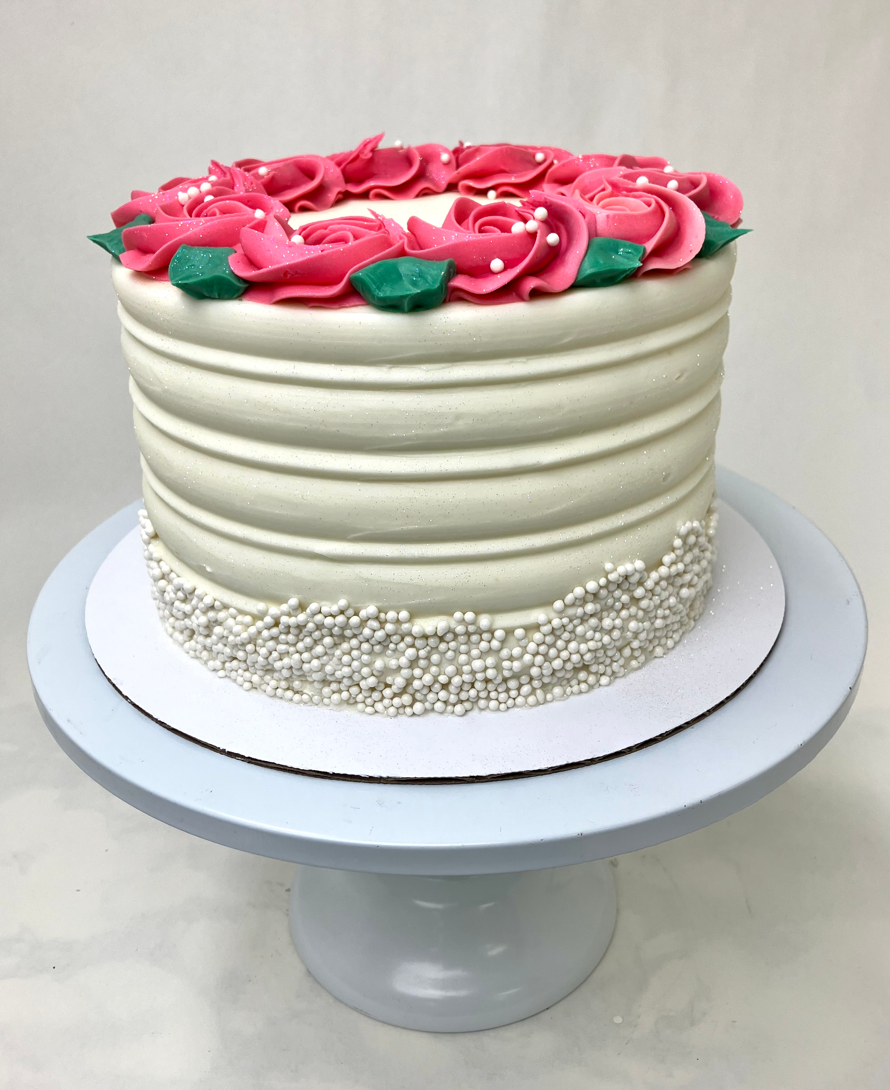 White cake with pink roses, green leaves, and sprinkles