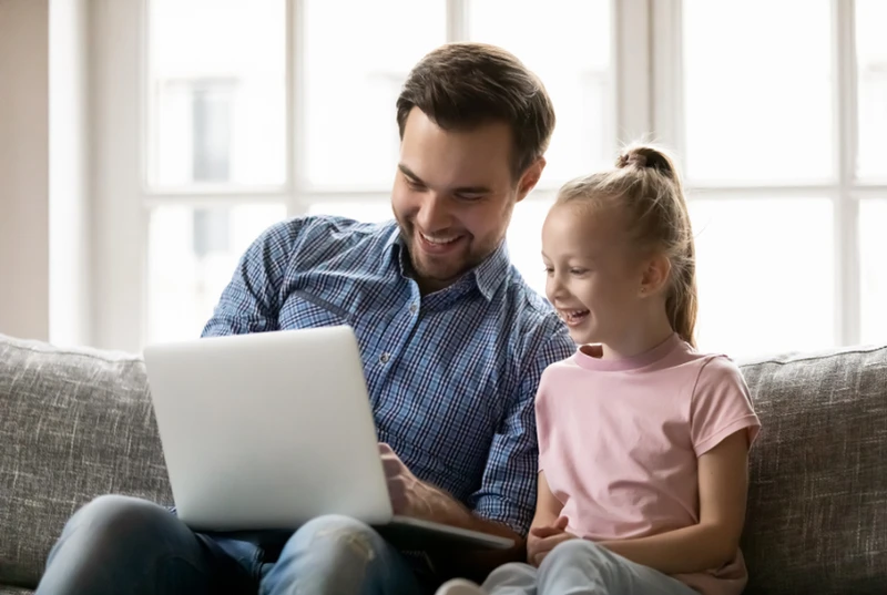 Smiling Dad showing his happy daughter something on a laptop